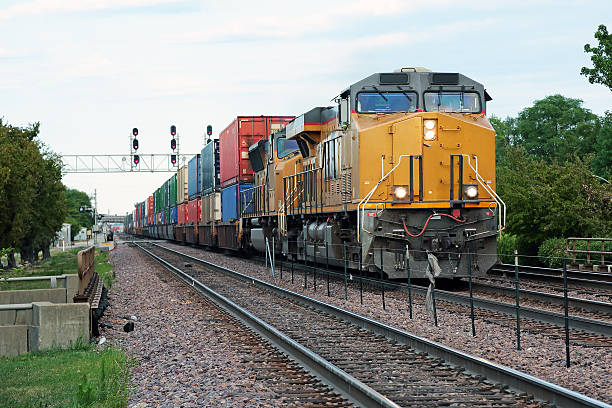 Two yellow locomotives and double stack freight train passing through town